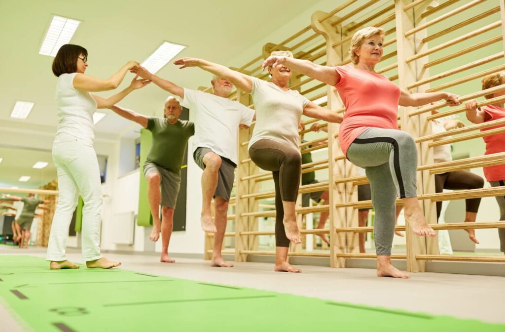 Seniors perform a Single Leg Stand in an exercise group, getting help from a trained staff member.