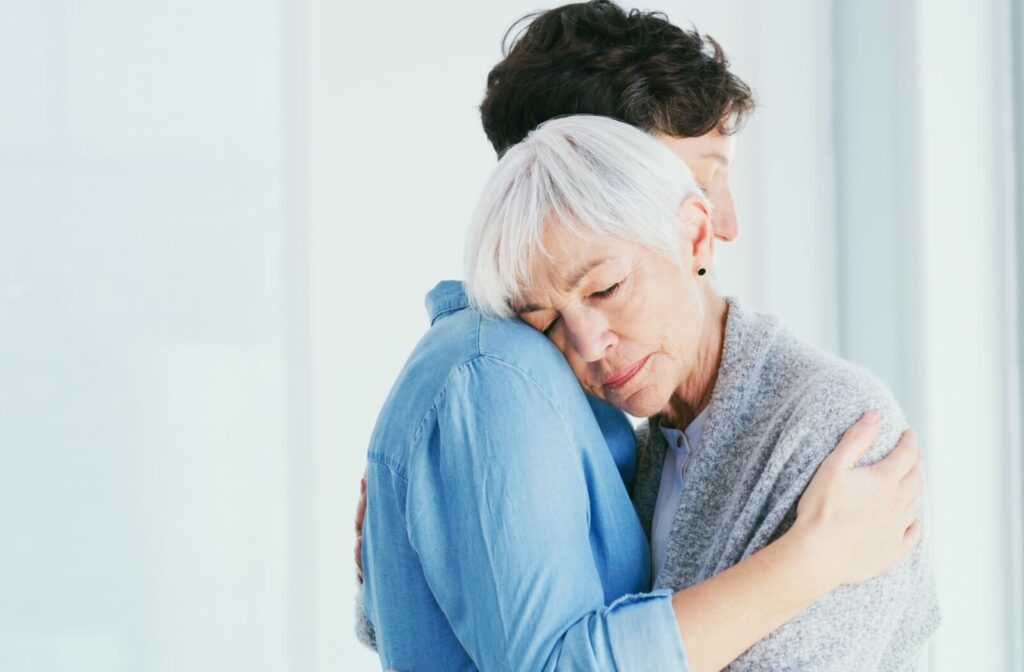 Older adult and younger person embracing with eyes closed in a quiet moment of comfort and emotional support