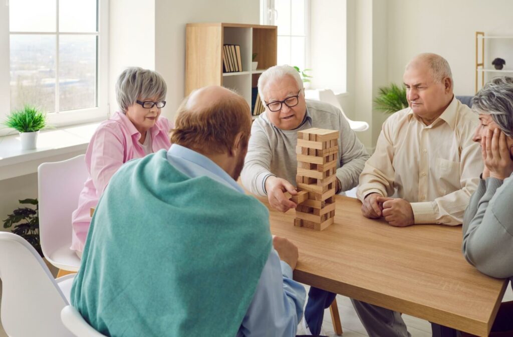 A group of seniors are sitting around a table and playing board games in an assisted living community.