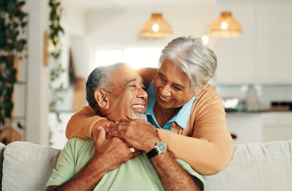 A senior couple smiles and embraces each other in a well-lit living room
